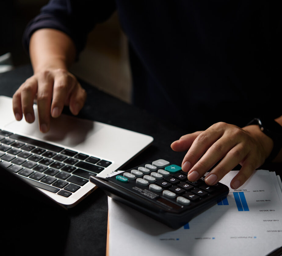 Professional accountant calculating tax expenses using calculator reviewing financial statement. Business finance expert performing budget analysis with modern accounting software and digital tools.